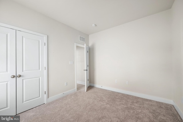 unfurnished bedroom with light colored carpet and a closet