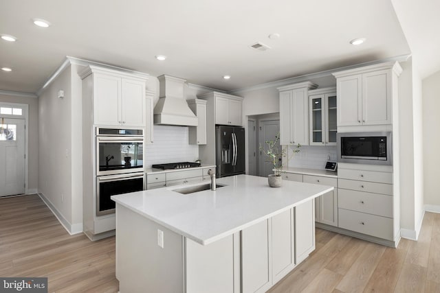 kitchen with sink, appliances with stainless steel finishes, white cabinetry, a center island with sink, and custom exhaust hood