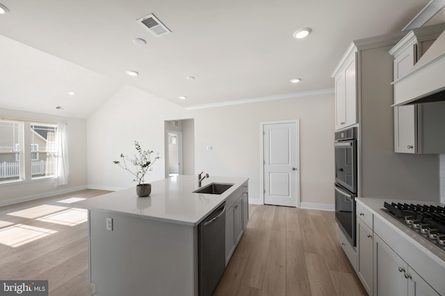 kitchen with an island with sink, sink, stainless steel appliances, custom range hood, and light hardwood / wood-style flooring