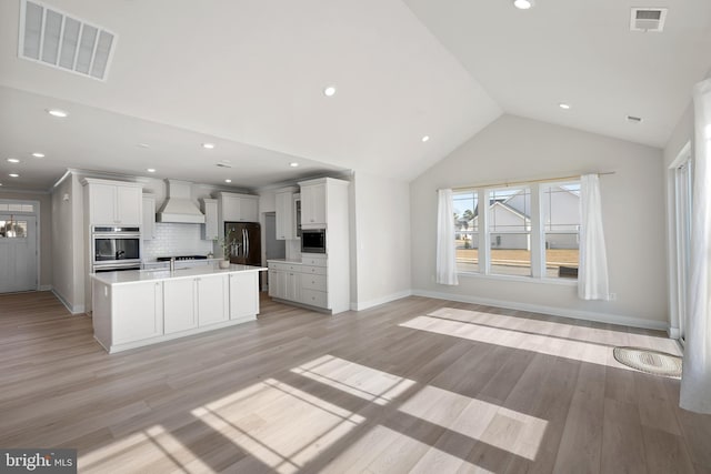 kitchen featuring custom exhaust hood, white cabinetry, a kitchen island with sink, and built in microwave