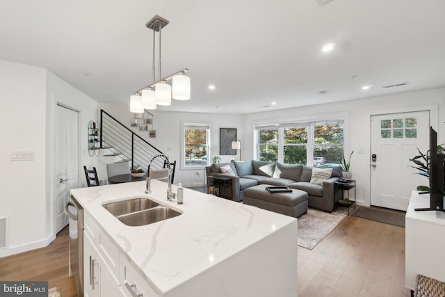 kitchen with a center island with sink, white cabinetry, sink, and pendant lighting