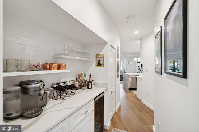 bar with wine cooler, light wood-type flooring, stainless steel dishwasher, light stone countertops, and white cabinets