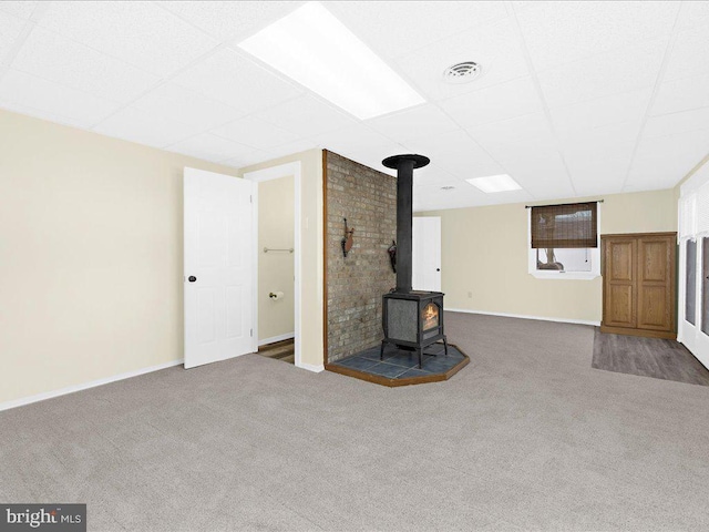 unfurnished living room featuring carpet flooring, a drop ceiling, and a wood stove