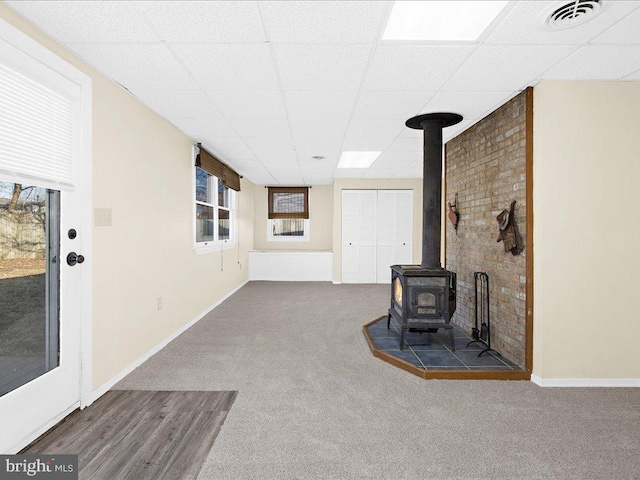 living room featuring carpet flooring, a paneled ceiling, and a wood stove