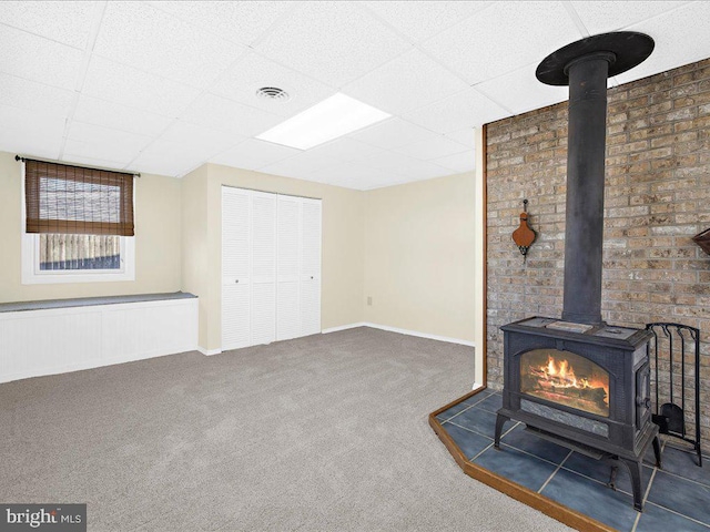 unfurnished living room featuring a drop ceiling, dark carpet, and a wood stove