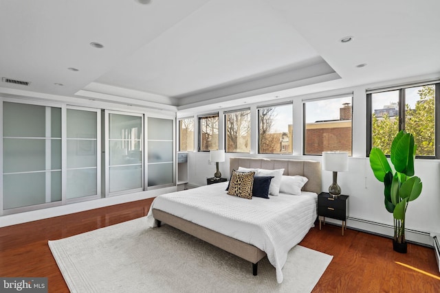 bedroom featuring multiple windows, dark wood-type flooring, and a tray ceiling