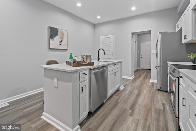 kitchen featuring sink, a center island with sink, appliances with stainless steel finishes, light hardwood / wood-style floors, and white cabinets