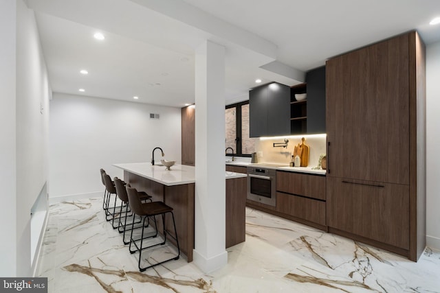 kitchen featuring backsplash, a breakfast bar area, an island with sink, and stainless steel oven