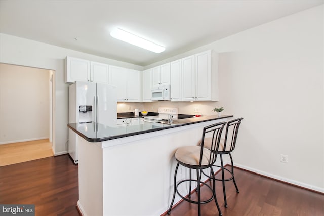 kitchen featuring a breakfast bar, white cabinetry, dark hardwood / wood-style floors, kitchen peninsula, and white appliances