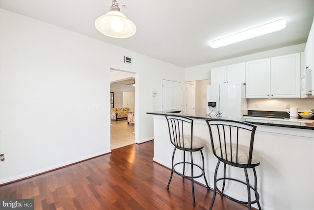 kitchen featuring decorative light fixtures, white cabinetry, a kitchen bar, white refrigerator with ice dispenser, and dark wood-type flooring