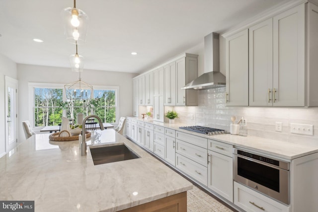 kitchen with light stone counters, wall chimney range hood, decorative light fixtures, and sink