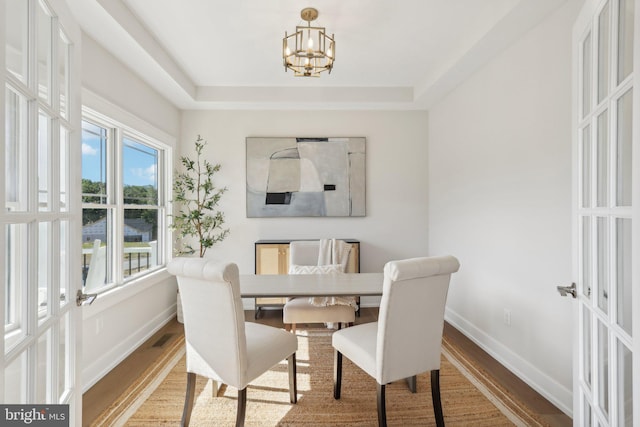 dining area featuring hardwood / wood-style flooring, a raised ceiling, an inviting chandelier, and french doors