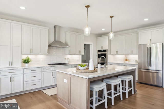 kitchen with white cabinetry, a center island with sink, wall chimney exhaust hood, and appliances with stainless steel finishes