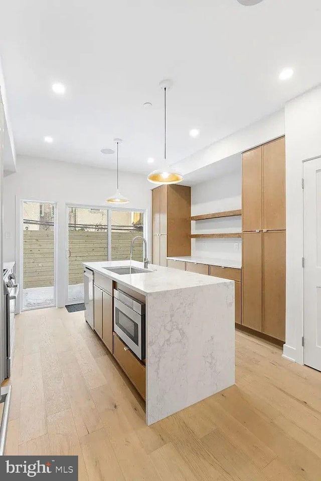 kitchen with pendant lighting, sink, light hardwood / wood-style flooring, appliances with stainless steel finishes, and a kitchen island with sink