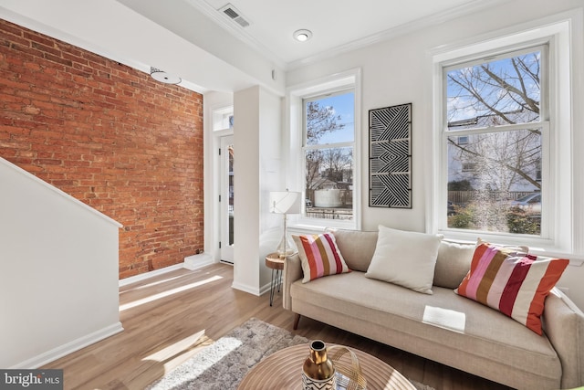 living area with brick wall, ornamental molding, plenty of natural light, and light hardwood / wood-style floors