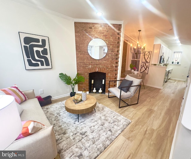 living room featuring ornamental molding, a notable chandelier, a fireplace, and light hardwood / wood-style floors