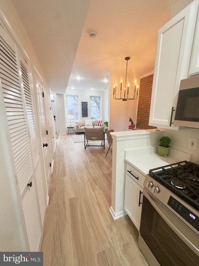 kitchen with hanging light fixtures, light wood-type flooring, white cabinets, and appliances with stainless steel finishes