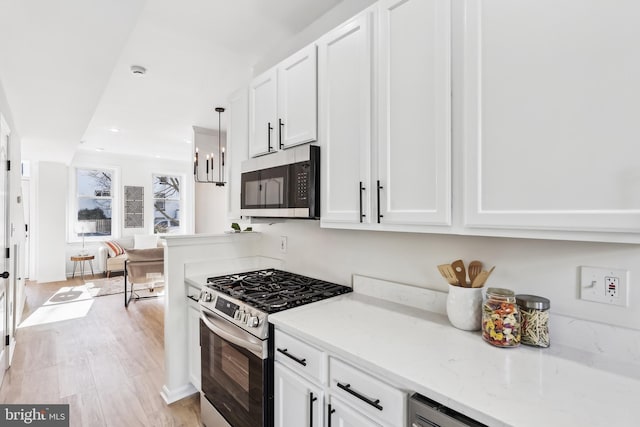 kitchen featuring stainless steel appliances, light stone countertops, white cabinets, and light hardwood / wood-style floors