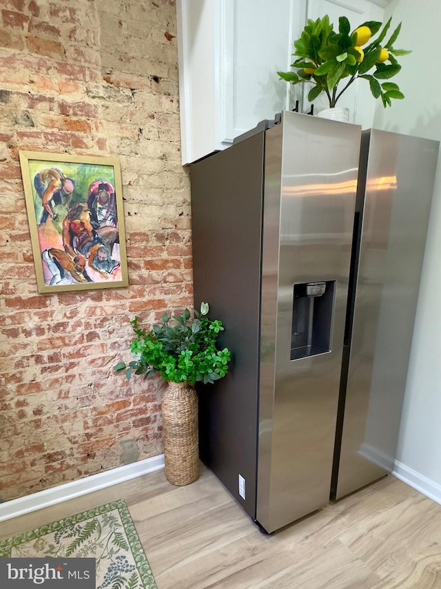 kitchen with brick wall, stainless steel fridge, and light hardwood / wood-style floors