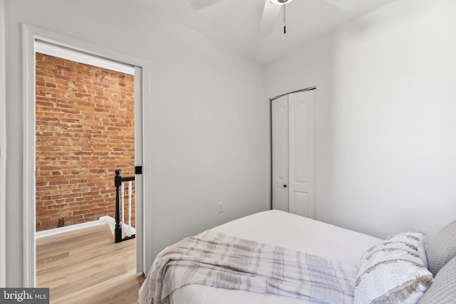 bedroom with light hardwood / wood-style floors, a closet, ceiling fan, and brick wall