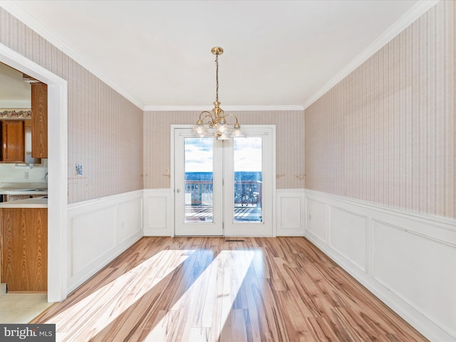 unfurnished dining area with a chandelier, a wainscoted wall, light wood finished floors, and wallpapered walls