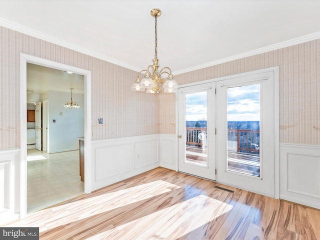 unfurnished dining area with wallpapered walls, light wood finished floors, wainscoting, ornamental molding, and a chandelier