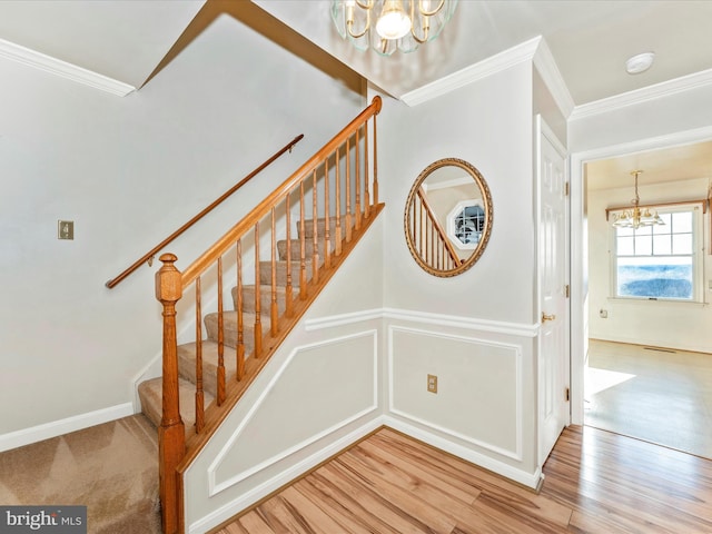 stairs with a chandelier, a decorative wall, wood finished floors, wainscoting, and crown molding