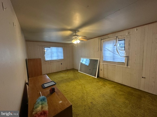 interior space with carpet flooring, ceiling fan, and wood walls