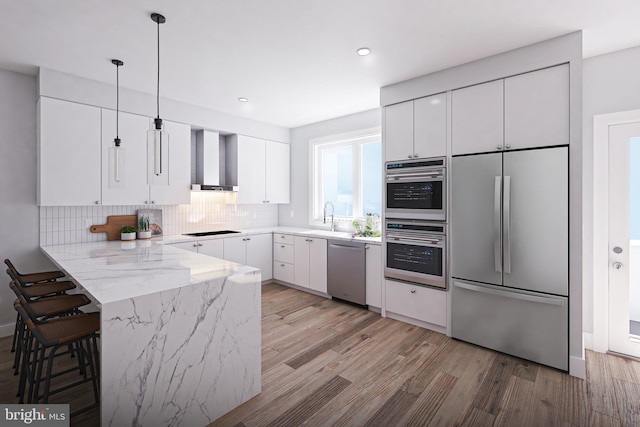 kitchen featuring white cabinetry, wall chimney range hood, kitchen peninsula, and appliances with stainless steel finishes