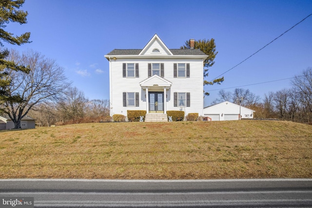 view of front of home featuring a detached garage, a chimney, and a front yard