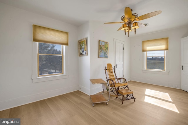 living area with light wood-type flooring, a ceiling fan, and baseboards