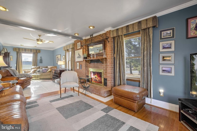 living area with crown molding, light wood-style floors, a ceiling fan, a brick fireplace, and baseboards