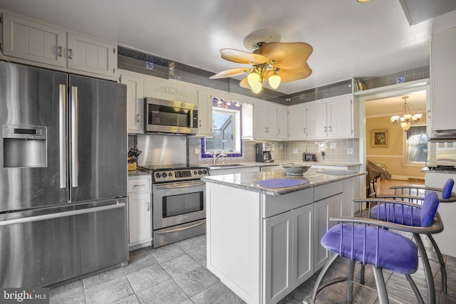 kitchen with tasteful backsplash, a kitchen island, light stone countertops, stainless steel appliances, and white cabinetry