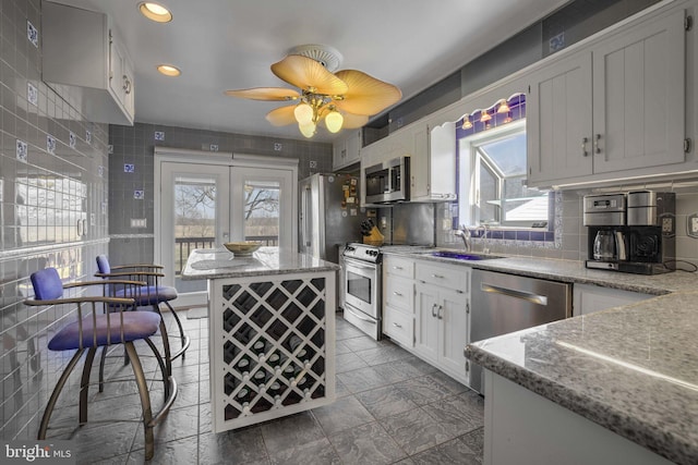 kitchen featuring appliances with stainless steel finishes, a sink, light stone counters, and white cabinets