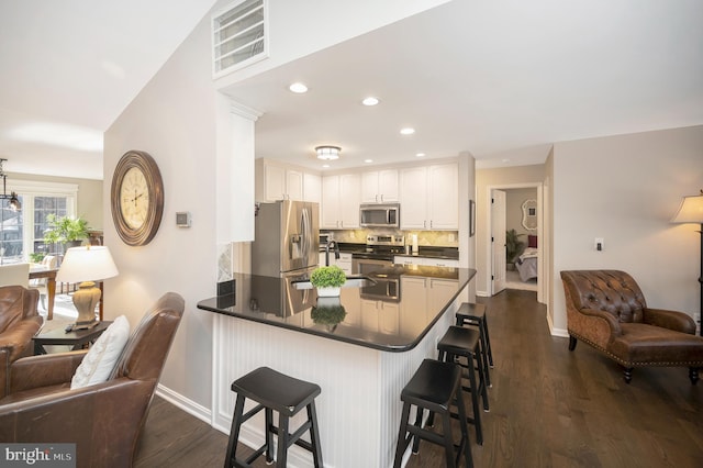 kitchen with appliances with stainless steel finishes, white cabinets, a kitchen bar, decorative backsplash, and kitchen peninsula