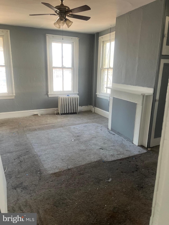 unfurnished living room with a wealth of natural light, carpet flooring, radiator heating unit, and ceiling fan