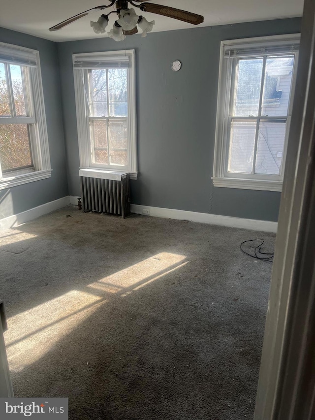 carpeted spare room with ceiling fan, radiator heating unit, and a wealth of natural light