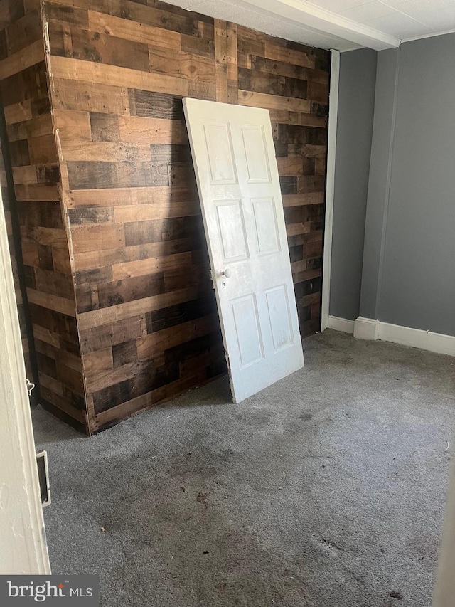 unfurnished room featuring wooden walls and dark colored carpet