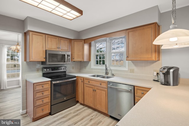 kitchen featuring a sink, light wood-style floors, light countertops, appliances with stainless steel finishes, and decorative backsplash