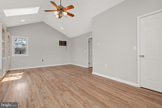 interior space with vaulted ceiling with skylight, a ceiling fan, light wood-style flooring, and baseboards