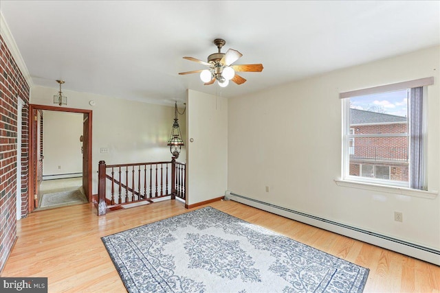 empty room featuring brick wall, a baseboard heating unit, and light hardwood / wood-style floors