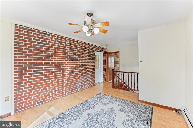 unfurnished room featuring light wood-type flooring, brick wall, and baseboard heating