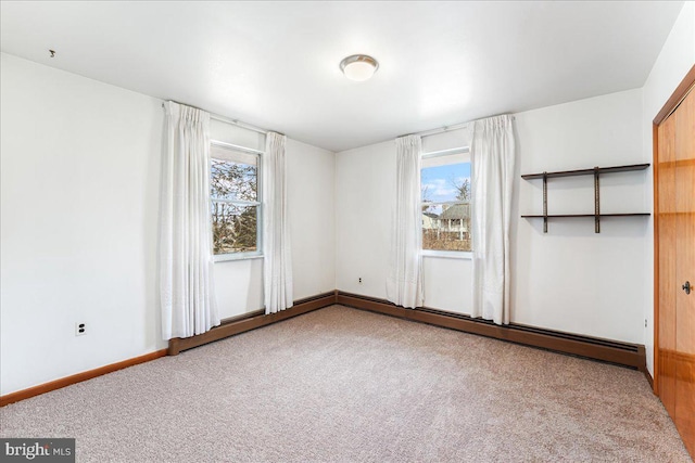 empty room with a baseboard heating unit, carpet floors, and plenty of natural light