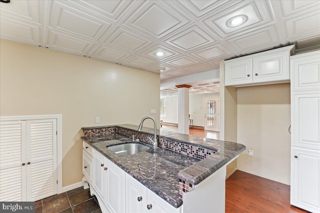 kitchen with dark stone countertops, kitchen peninsula, sink, and white cabinets