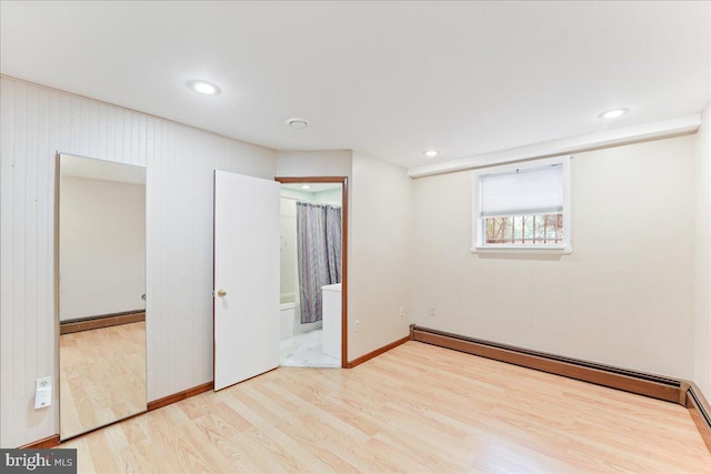 unfurnished bedroom with a baseboard radiator, ensuite bathroom, and light wood-type flooring