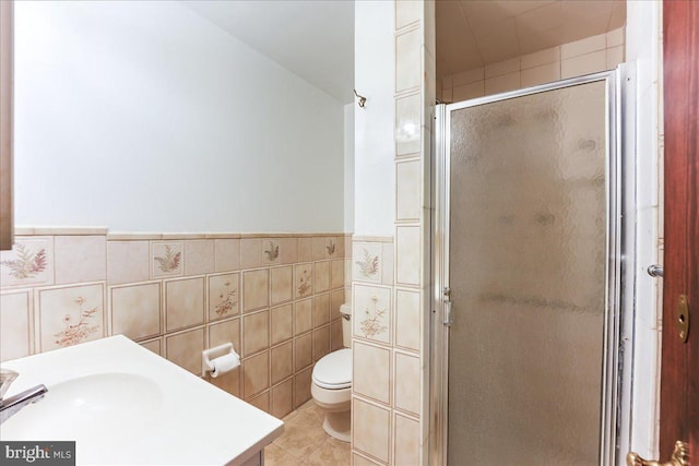 bathroom with a shower with shower door, tile walls, vanity, toilet, and tile patterned floors