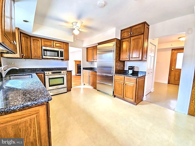 kitchen featuring dark stone countertops, sink, stainless steel appliances, and ceiling fan