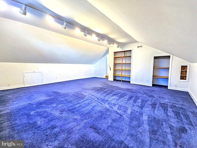 bonus room featuring lofted ceiling, dark carpet, and built in shelves