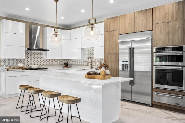 kitchen with wall chimney exhaust hood, white cabinetry, a center island, pendant lighting, and stainless steel appliances