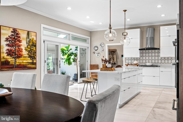 kitchen with pendant lighting, white cabinets, decorative backsplash, ornamental molding, and wall chimney exhaust hood